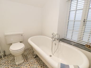 A bathroom with a toilet and a freestanding bathtub next to a window with blinds at Pentowyn in Holyhead