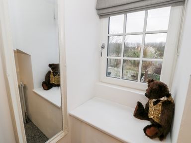 A teddy bear wearing a vest sitting on a window ledge next to a window with a large mirror on the wall at Pentowyn in Holyhead