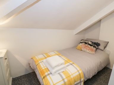 A small bedroom with a single bed a yellow plaid blanket folded towels on the bed and a white cabinet at Pentowyn in Holyhead