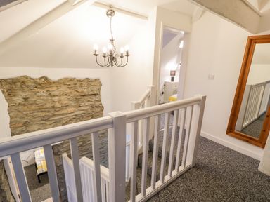 A staircase with white banisters leading to a hallway with a bedroom and a wall mirror at Pentowyn in Holyhead