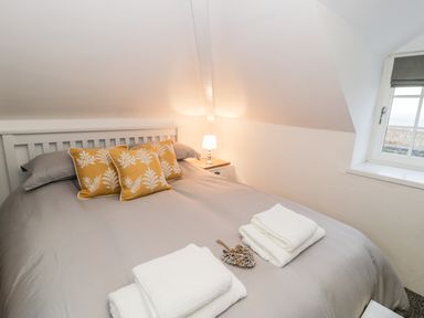A bedroom with a bed with yellow pillows and folded white towels on it at Pentowyn in Holyhead