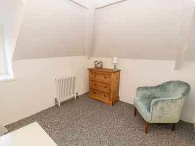 A room with a wooden chest of drawers with a lamp and decoration and a green upholstered armchair at Pentowyn in Holyhead
