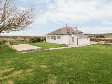 A single story house with a red tiled roof and white walls surrounded by a large grassy yard and a tree at Pentowyn in Holyhead