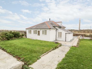 A white house with a slate roof and a grassy yard at Pentowyn in Holyhead