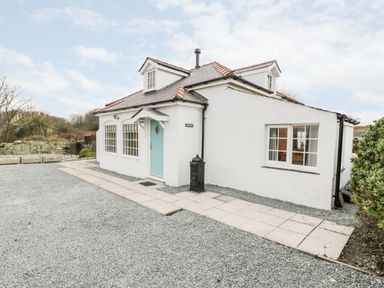 A white house with a blue door and two dormer windows on a gravel driveway at Pentowyn in Holyhead