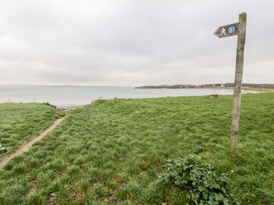 A grassy area with a walking path and wooden signpost near a body of water at Pentowyn in Holyhead