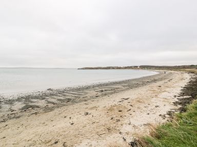 A sandy beach with seaweed and calm water under a cloudy sky at Pentowyn in Holyhead