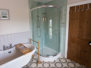 A bathroom with a clawfoot bathtub a glass shower enclosure and a wooden door at Moelwyn View Cottage in Llan Ffestiniog