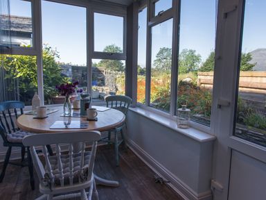 A dining area with a round wooden table and chairs near windows showing a garden at Moelwyn View Cottage in Llan Ffestiniog