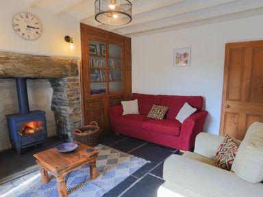A living room with a red sofa a beige armchair a wooden coffee table and a fireplace at Moelwyn View Cottage in Llan Ffestiniog