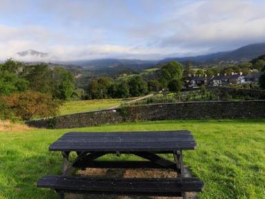 A wooden picnic table on grass with a stone wall cemetery and houses in the background at Moelwyn View Cottage in Llan Ffestiniog