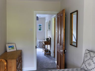 A hallway with a wooden dresser and framed picture leading to another room with a laundry basket and small table at Moelwyn View Cottage in Llan Ffestiniog