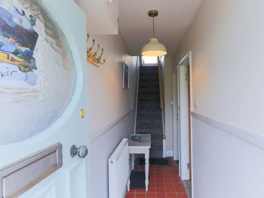 A hallway with a staircase carpeted in dark grey a small table under a hanging light and a coat rack on the wall at Moelwyn View Cottage in Llan Ffestiniog