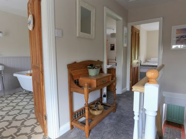 A hallway with a wooden side table a mirror and doors leading to a bathroom and bedrooms at Moelwyn View Cottage in Llan Ffestiniog