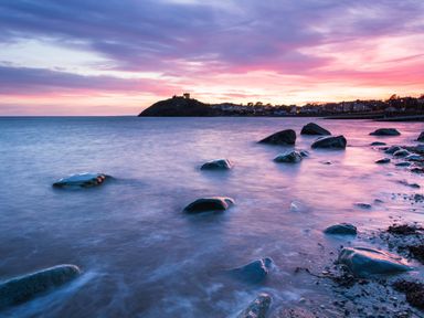 A rocky shoreline at sunset with a distant hill and buildings at Moelwyn View Cottage in Llan Ffestiniog