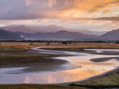 A winding river flowing through a flat marshland with mountains in the background at Moelwyn View Cottage in Llan Ffestiniog