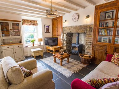 A living room with a stone fireplace and wood burning stove two sofas a wooden bookshelf and a television at Moelwyn View Cottage in Llan Ffestiniog