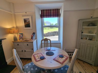 A dining area with a round wooden table and four chairs by a window showing a hill at Moelwyn View Cottage in Llan Ffestiniog