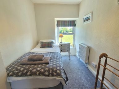 A small bedroom with a single bed a side table lamp window with a view and a radiator at Moelwyn View Cottage in Llan Ffestiniog