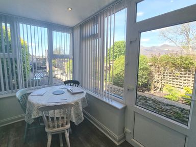 A dining area with a round table and three chairs next to large windows and a glass door at Moelwyn View Cottage in Llan Ffestiniog
