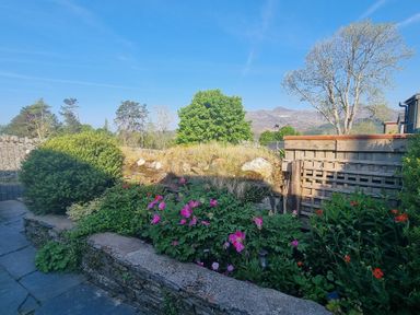 A garden with flowers bushes and trees with mountains in the background at Moelwyn View Cottage in Llan Ffestiniog