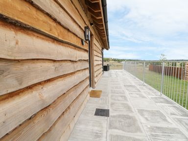 An outdoor tiled patio with wooden siding and metal railing overlooking a grassy area at Swan Lodge Castle Farm in Wedmore
