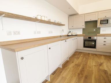 A kitchen with wooden countertops white and grey cabinets a built in oven microwave kettle toaster and open wooden shelf at Swan Lodge Castle Farm in Wedmore