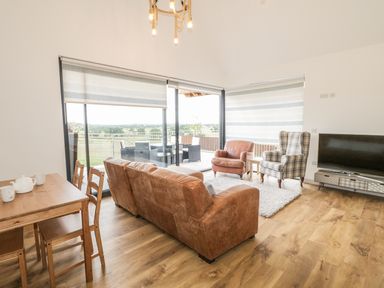 A living room with leather sofa armchairs a television and wooden dining table near large windows at Swan Lodge Castle Farm Wedmore