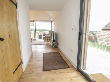 A hallway with wooden floor and rug leading to a living room with chairs and a TV at Swan Lodge Castle Farm in Wedmore
