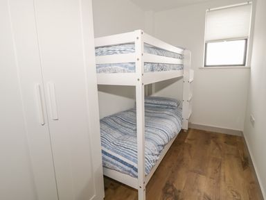 A small bedroom with a white bunk bed and a wardrobe with wooden flooring at Swan Lodge Castle Farm in Wedmore