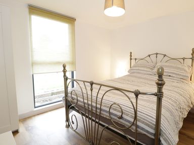 A bedroom with a metal bed frame and striped bedding with a window and roller blind at Swan Lodge Castle Farm Wedmore