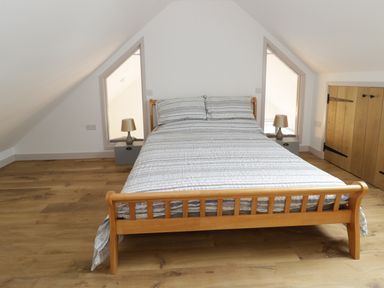 A bedroom with a wooden bed and striped bedding between two triangular windows with lamps on side tables at Swan Lodge Castle Farm in Wedmore