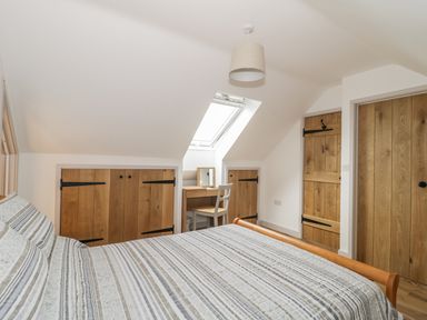A bedroom with a bed a desk and chair under a skylight and wooden doors at Swan Lodge Castle Farm in Wedmore