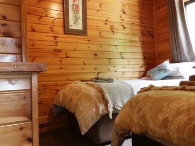 A bedroom with wooden walls two beds with blankets and towels and a framed floral picture on the wall at Oak Lodge Constantine near Falmouth