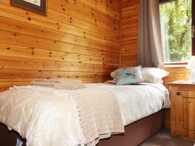 A bedroom with a single bed beige bedding wooden walls and a window at Oak Lodge in Constantine near Falmouth