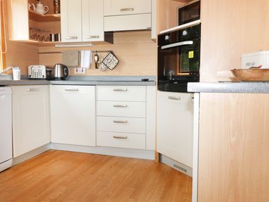 A kitchen with white cabinets a toaster kettle oven and bread bin at Oak Lodge in Constantine near Falmouth