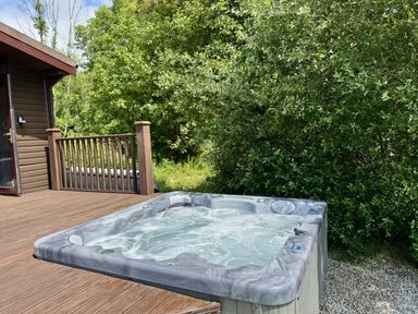 A hot tub on a deck surrounded by trees at Willow Lodge in Constantine near Falmouth