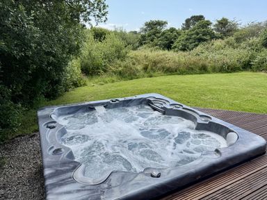 A hot tub on decking in a garden at Willow Lodge in Constantine near Falmouth