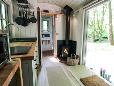 A compact kitchen area with wooden countertops pots and pans hanging and a stove next to a wood burning stove at Rock View Shepherd's Hut in Gulworthy near Tavistock