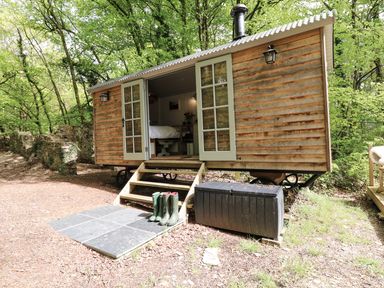 A wooden shepherd's hut with open doors and boots outside in a forest area at Rock View Shepherd's Hut Gulworthy near Tavistock