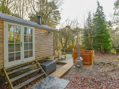 A wooden hut with glass double doors next to a deck with chairs and a wooden hot tub at Rock View Shepherd's Hut in Gulworthy near Tavistock