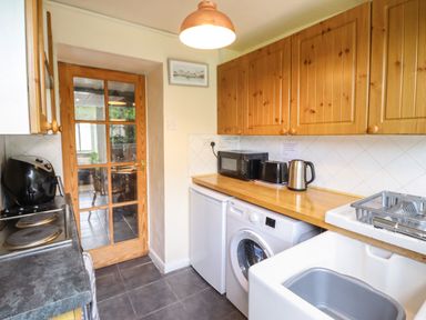 A kitchen with wooden cabinets a washing machine a mini fridge microwave toaster kettle and a sink at Gwenallt in Malltraeth