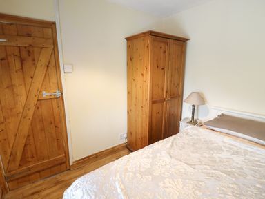 A bedroom with a wooden wardrobe a bedside table with lamp and a bed at Gwenallt in Malltraeth