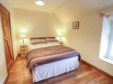 A bedroom with a double bed flanked by two bedside tables with lamps and a window to the right at Gwenallt in Malltraeth