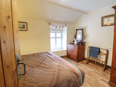 A bedroom with a bed a wooden dresser with a mirror a window and a towel rack at Gwenallt in Malltraeth