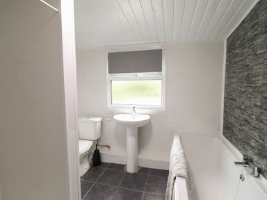 A bathroom with a toilet sink bathtub towel and a window with a blind at Gwenallt in Malltraeth