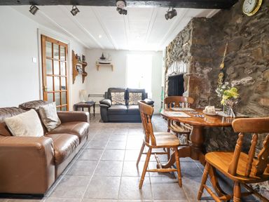A living room with leather sofas a wooden dining table and chairs a stone wall and a glass door at Gwenallt in Malltraeth