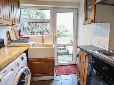A kitchen with a washing machine sink and oven next to a door leading outside at Gwenallt in Malltraeth