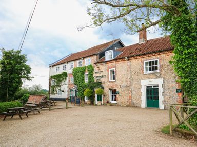Exterior of a brick building with green foliage ivy and outdoor wooden benches at Culthorpe Mill in Hempton near Fakenham