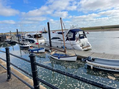 A marina with several boats docked along a wooden pier and a metal railing in the foreground at Springfield in Hempton near Fakenham